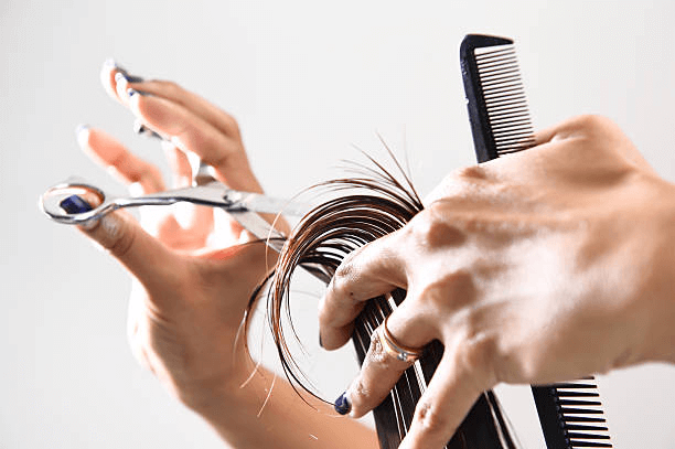 a professional holding a comb in her left hand and scissors in her right hand giving a haircut to a brunette 