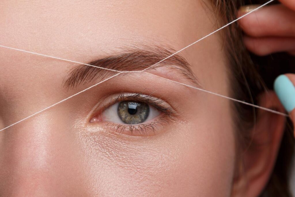 A woman holds thin threads up to her eyebrow before removing unwanted hair with eyebrow threading.