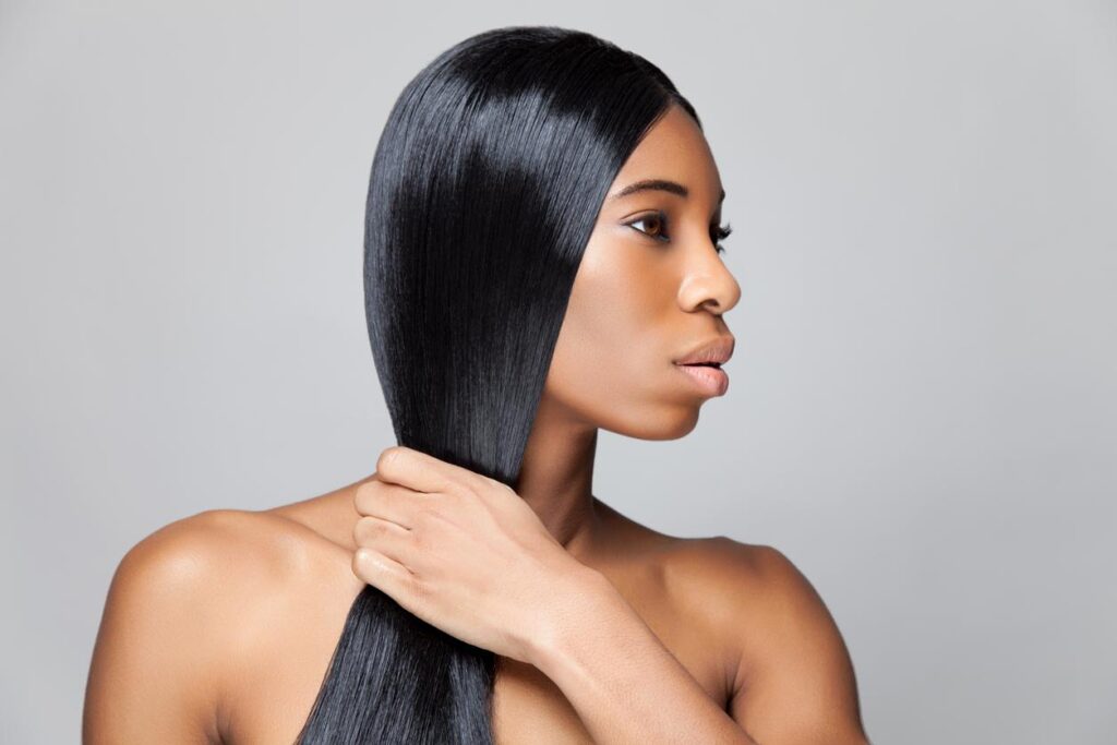 Woman with straight, long, sleek black hair. She is gripping her hair with one hand in front of her body.